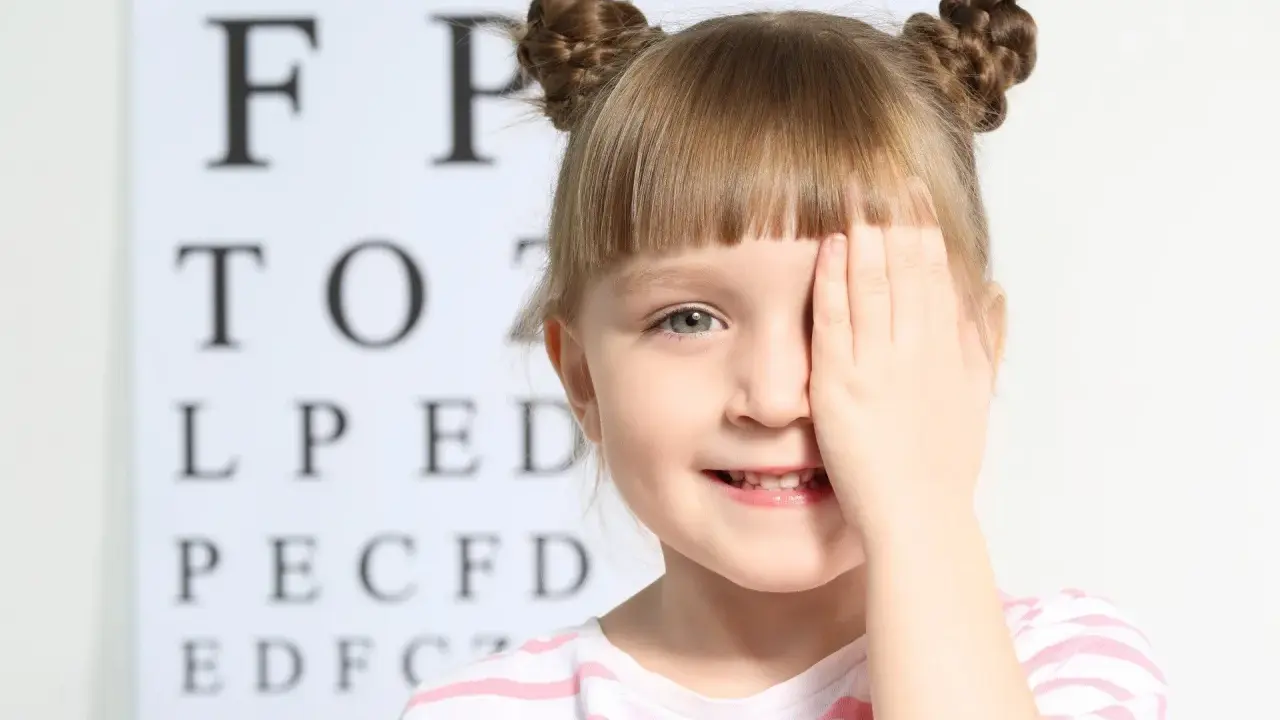 Mała dziewczynka zasłania oko ręką podczas badania wzroku. Czy to początek krótkowzroczności u dzieci?