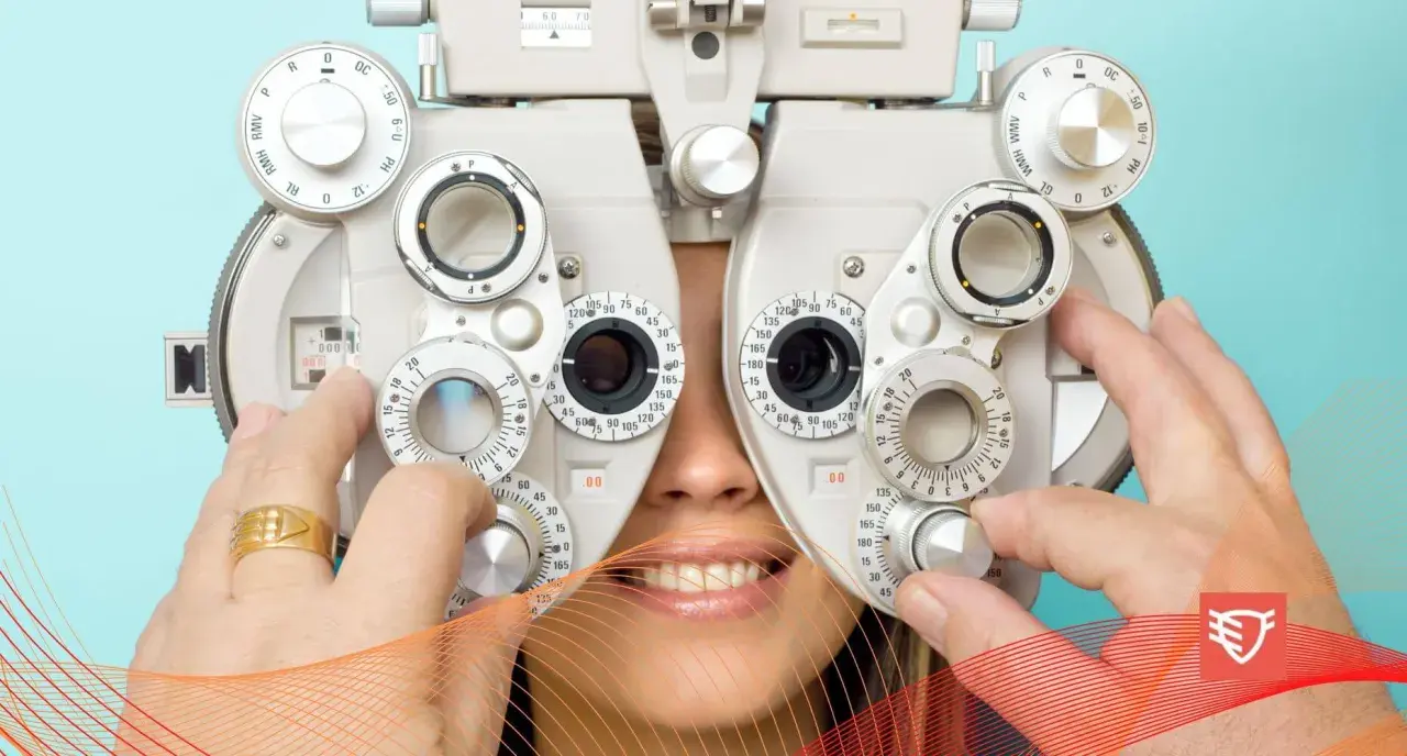 Badanie optometryczne: pacjent uśmiecha się, gdy optometrysta reguluje soczewki refraktora.