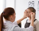 Okulista wykonuje ćwiczenia na akomodację oka u dziewczynki, zasłaniając jej jedno oko.