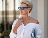 Elegancka starsza pani w okularach i białej koszuli, z biżuterią.
