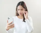 Kobieta z okularami próbuje odczytać coś na telefonie, marszcząc brwi. Może to być objaw astygmatyzmu krótkowzrocznego.