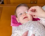 Delikatne przemywanie oka niemowlaka wacikiem. Pielęgnacja oczu dziecka jest ważna.