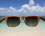 Drewniane okulary przeciwsłoneczne z filtrem uv 3 chronią oczy na plaży. W tle błękitne niebo i turkusowe morze.