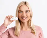 Uśmiechnięta blondynka trzyma pojemniczek z soczewkami dla dalekowidza.