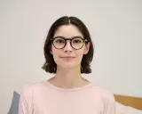 Kobieta w okularach z okrągłymi, ciemnymi oprawkami uśmiecha się. Jej wzrok jest bystry, jakby widziała wszystko doskonale, co oznacza 20:20.
