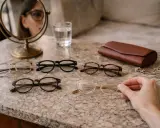 Wybieram okulary do chodzenia. Na blacie leżą cztery pary okularów, skórzane etui i biżuteria.