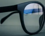 Okulary z czarnymi oprawkami, soczewki z niebieskim antyrefleksem odbijają światło.