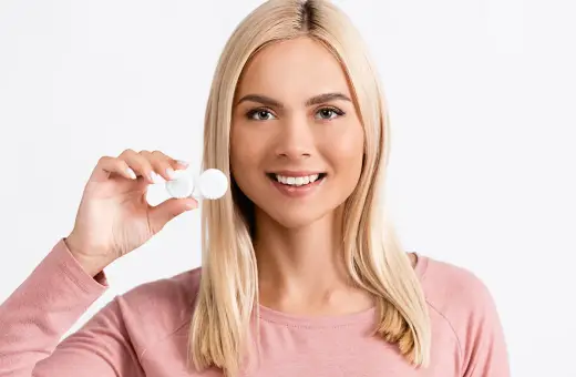 Uśmiechnięta blondynka trzyma pojemniczek z soczewkami dla dalekowidza.