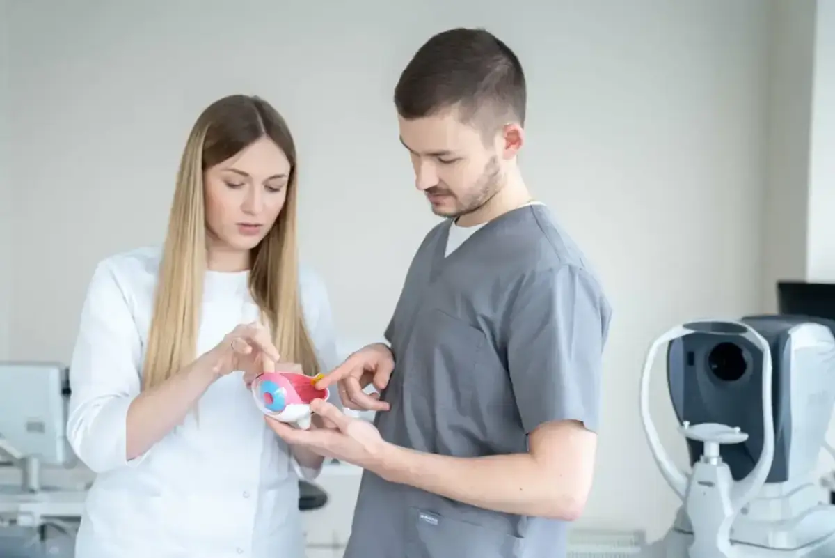 Lekarze omawiają model oka, zastanawiając się, czy wadę wzroku da się wyleczyć. W tle aparat do badania wzroku.
